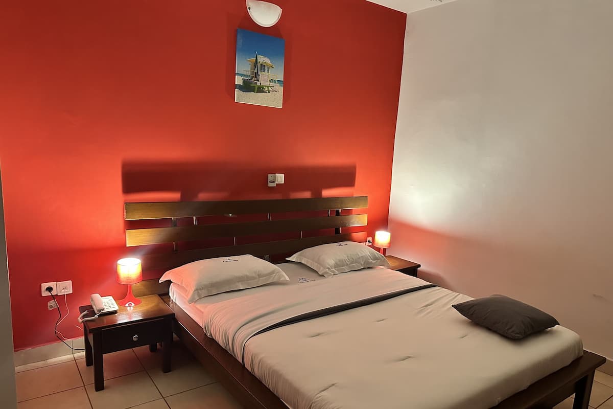 A hotel room with a wooden headboard, a bed with white bedding, two bedside tables with lamps, and a wall-mounted picture.