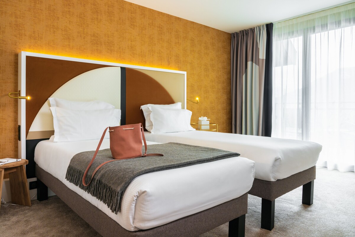 Une chambre d’hôtel avec un grand lit, une table de chevet, une lampe et une fenêtre avec des rideaux.
