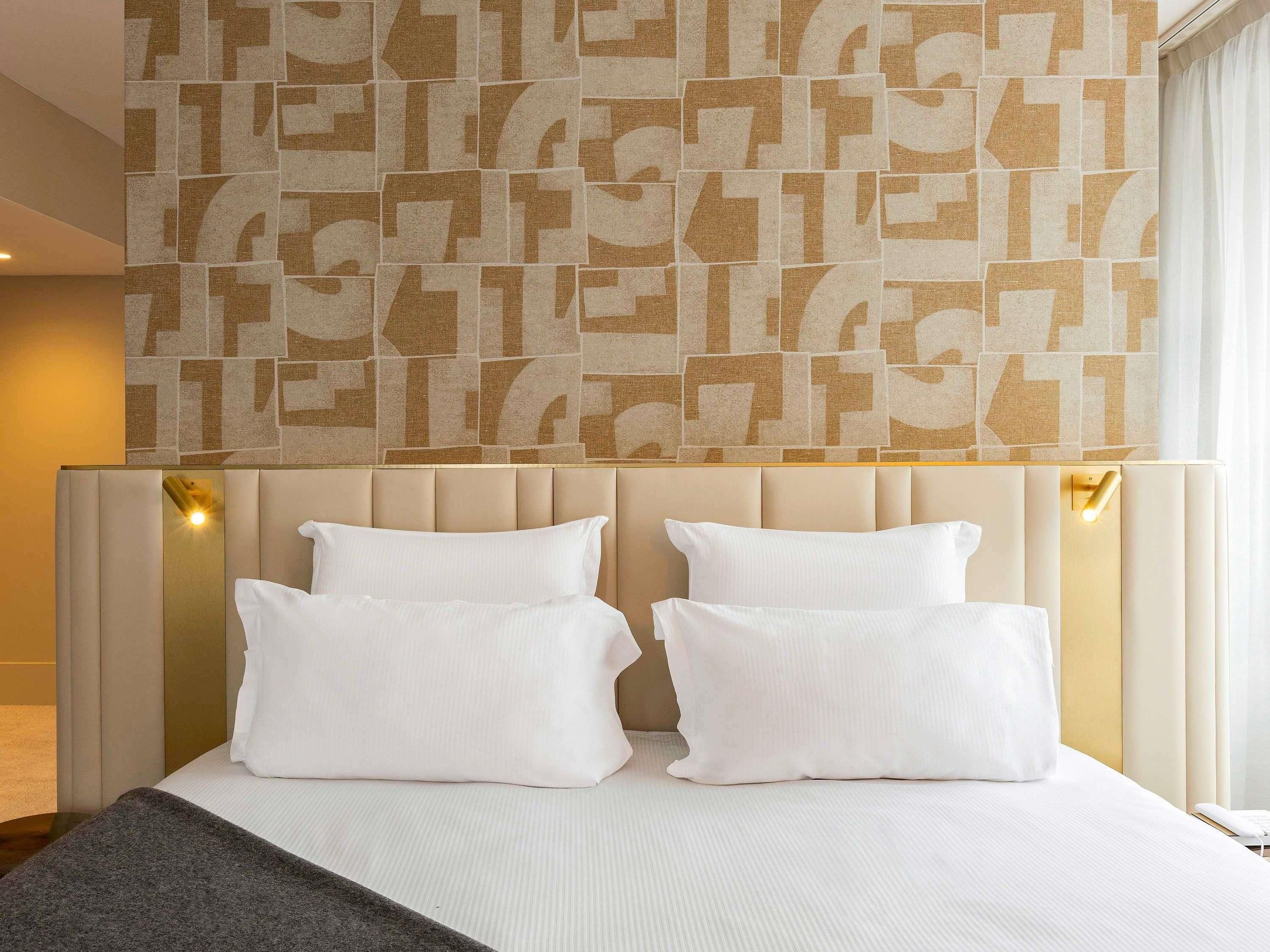Ein Hotelzimmer mit einem großen Bett, einem Kopfteil mit hellen Paneelen und einer geometrisch gemusterten Wand darüber.