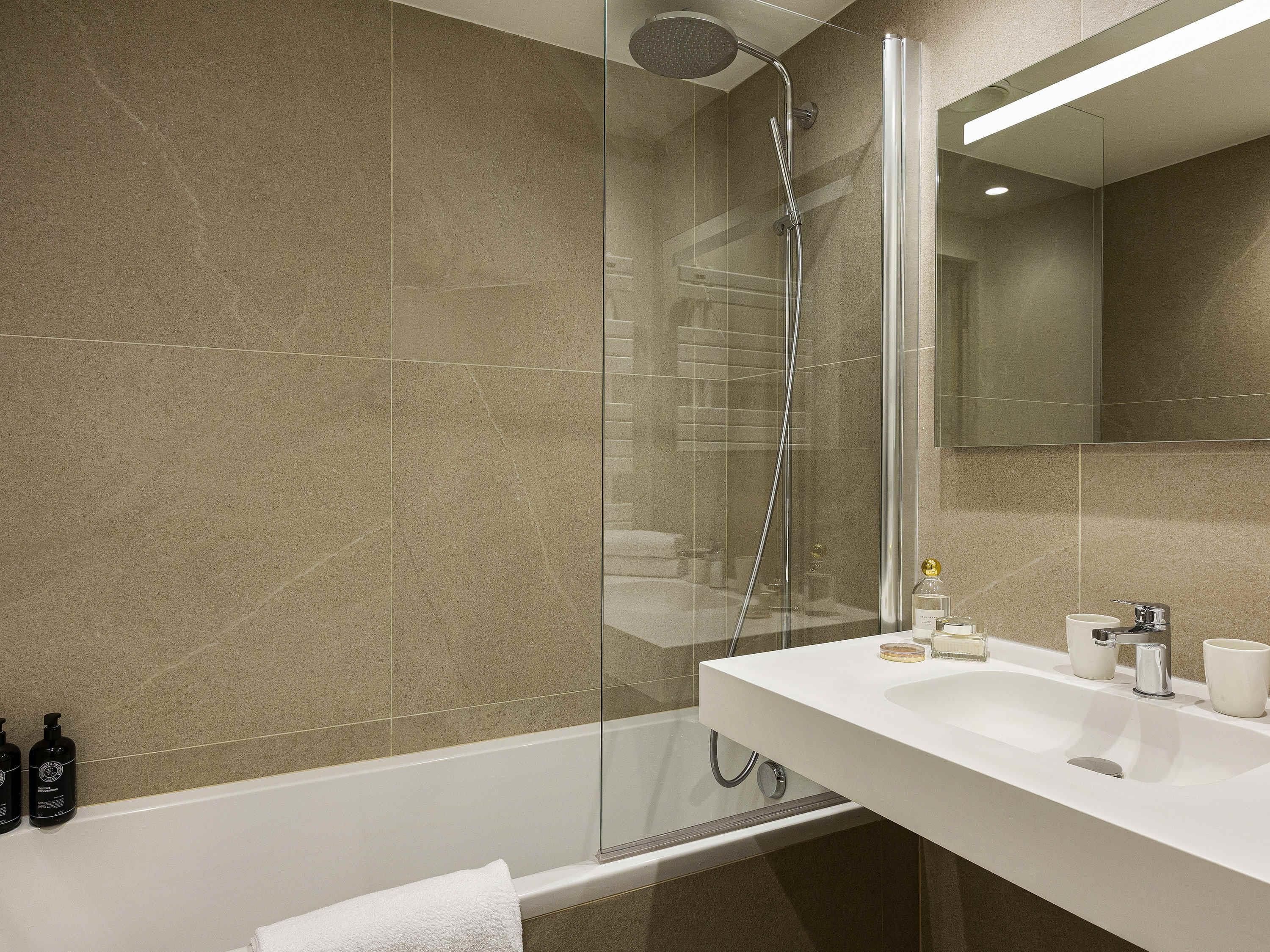 A modern bathroom with a glass-enclosed shower, a white sink, and a large mirror.