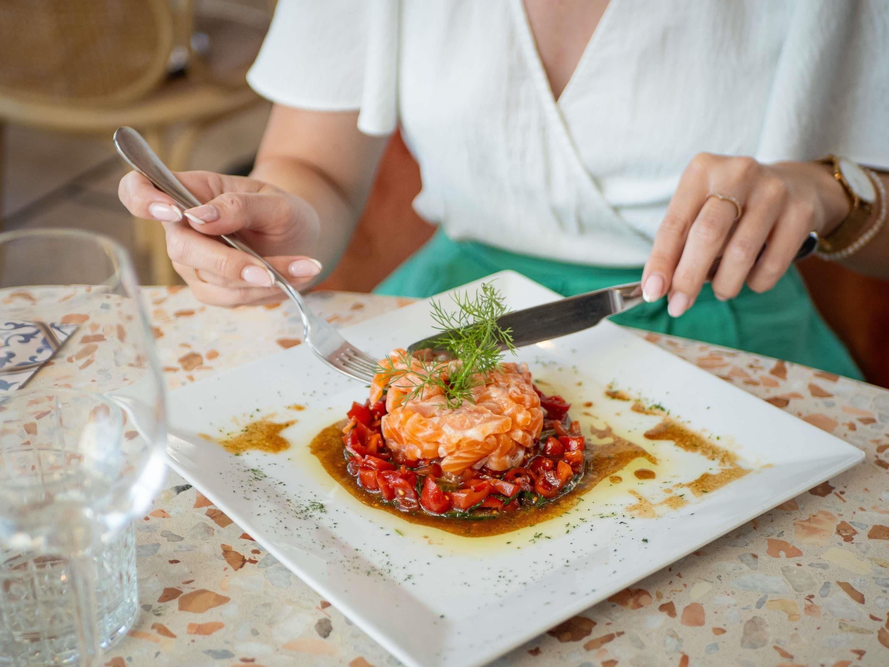 Una persona comiendo en una mesa, con un plato de comida, un tenedor y un cuchillo.