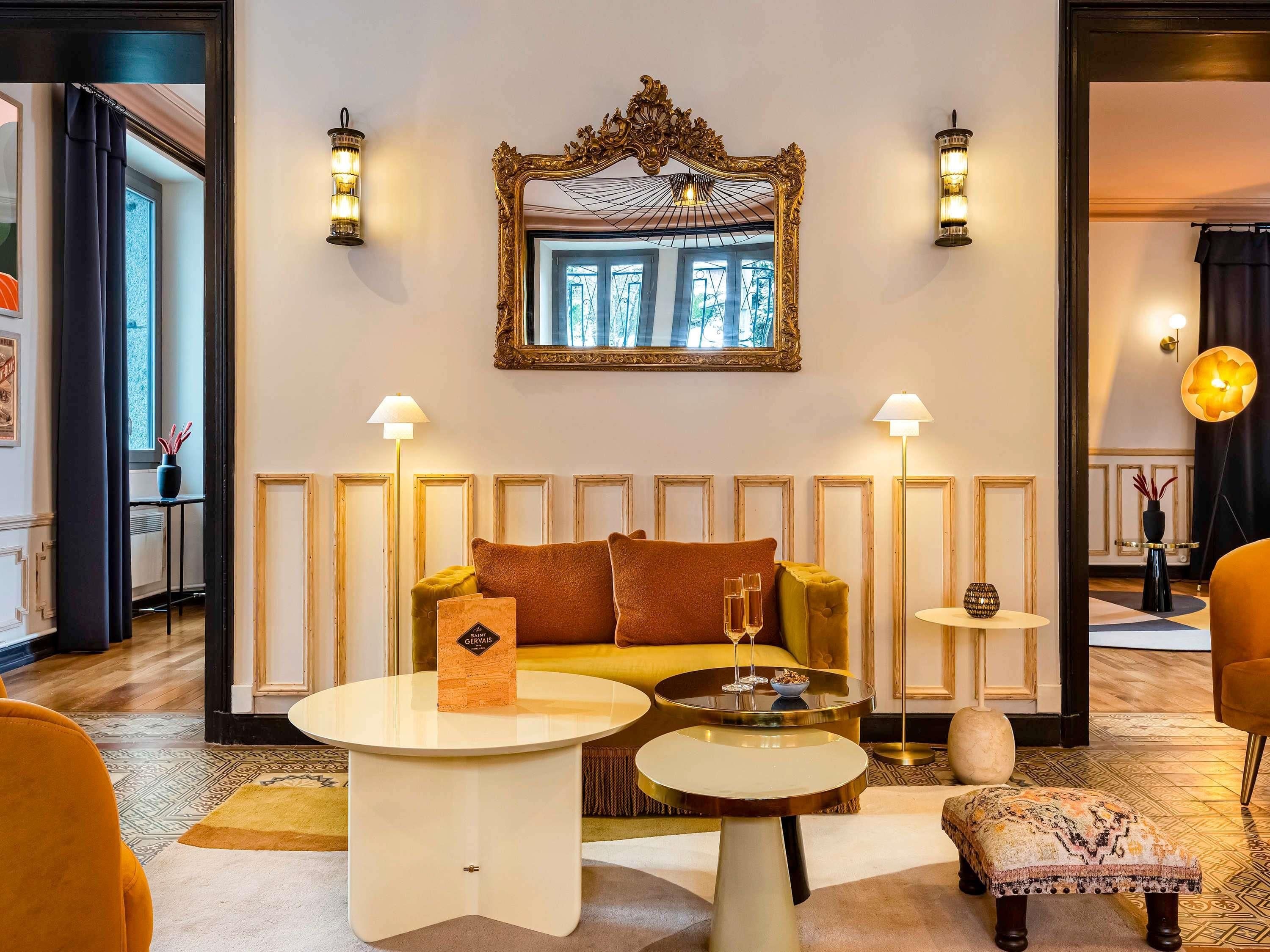 A room with a sofa, two round tables, a mirror, and wall sconces.