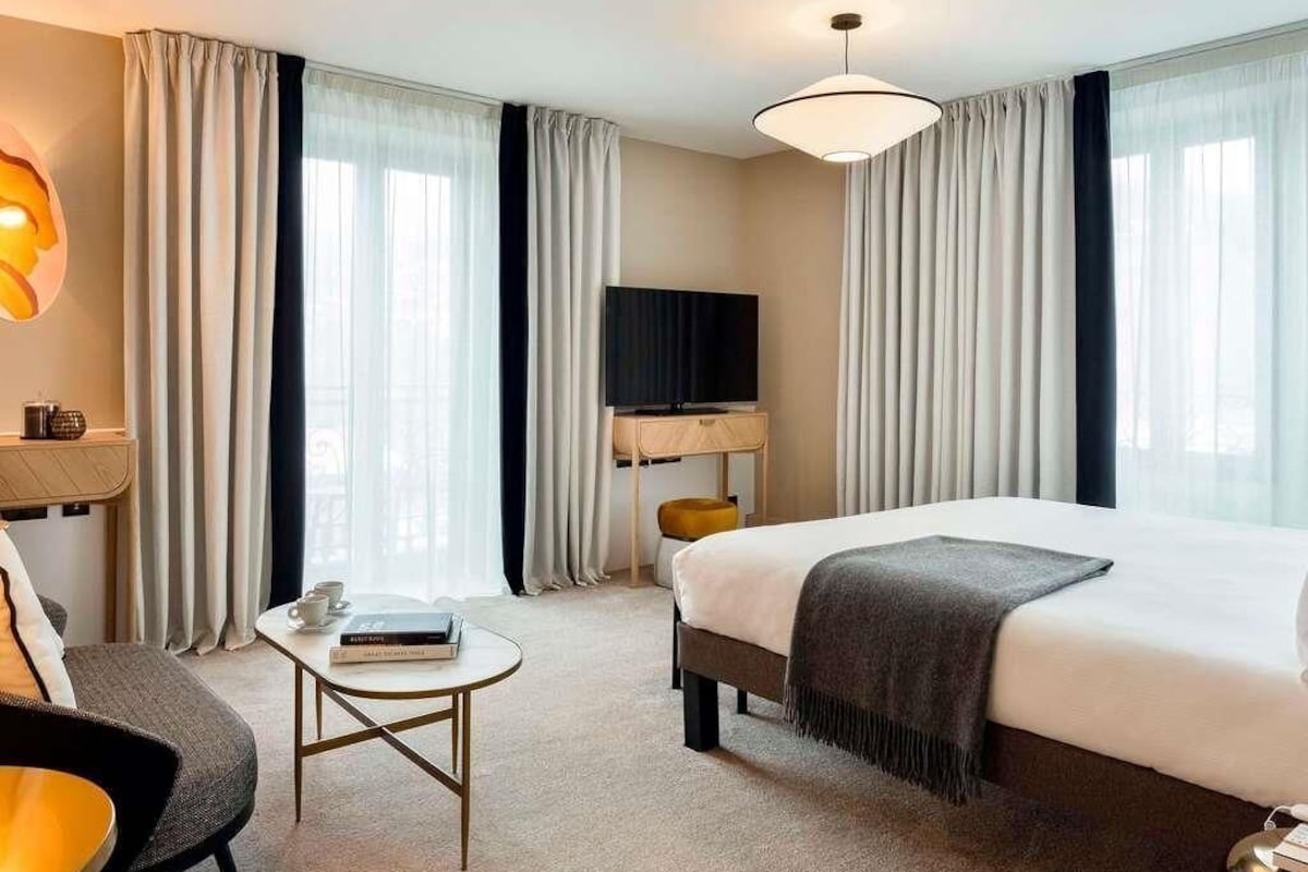 Une chambre d’hôtel avec un lit, une télévision, un bureau, une chaise et des rideaux.