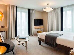 Une chambre d’hôtel avec un lit, une télévision, un bureau, une chaise et des rideaux.