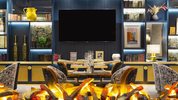 A modern living room with a fireplace, a large flat-screen TV, and a bookshelf filled with books and decorative items.