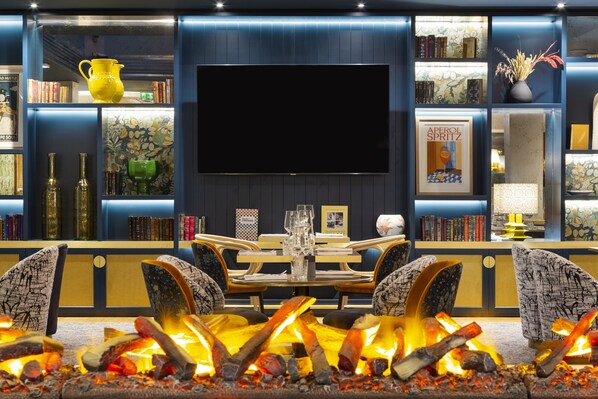 Un salon moderne doté d’une cheminée, d’un grand téléviseur à écran plat et d’une bibliothèque remplie de livres et d’objets décoratifs.