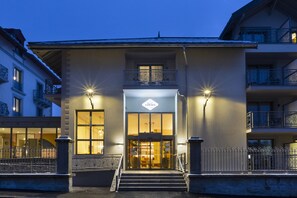 Entrada de hotel con puertas dobles, dos ventanas iluminadas y un balcón con barandilla.