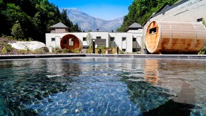 Una piscina cristalina con estructuras de madera con forma de barril y montañas al fondo.