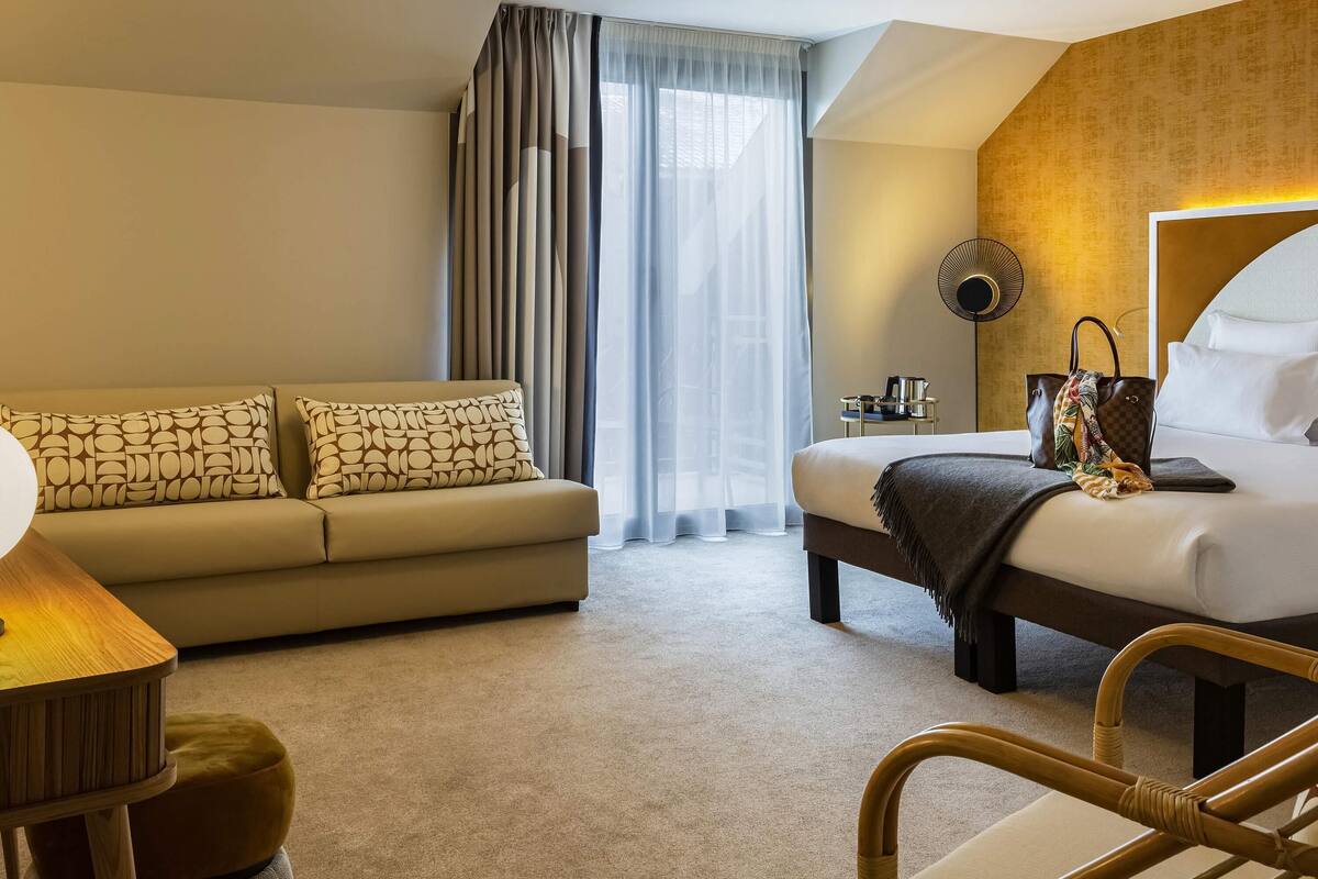 A modern hotel room with a sofa, bed, and a small table.