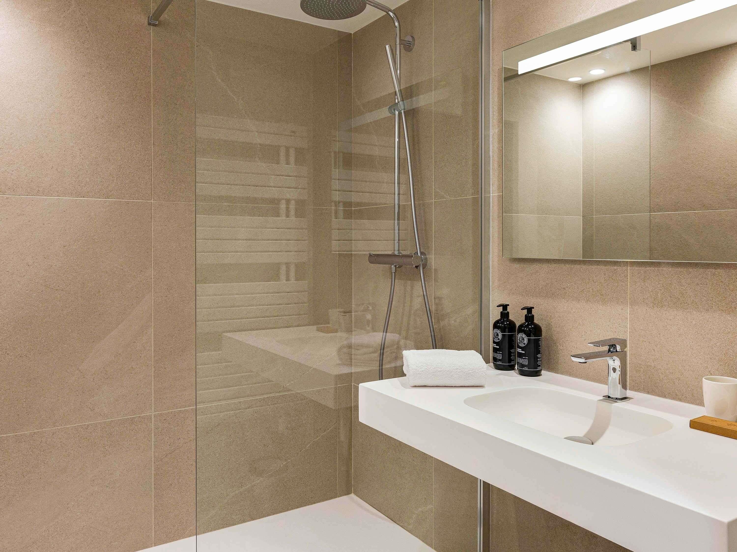 A modern bathroom with a glass shower enclosure, a white sink, and a mirror above it.