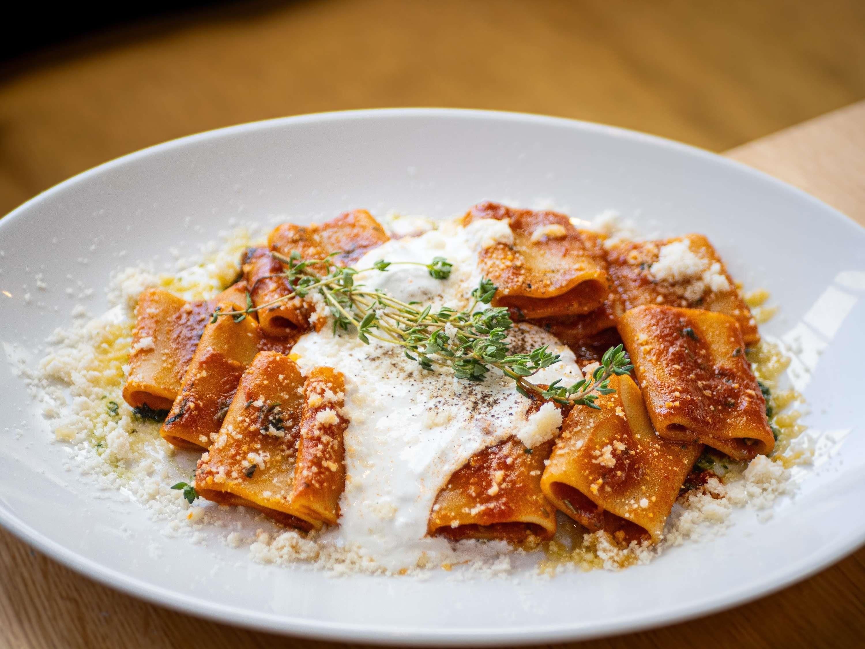 Een bord ravioli met saus, kaas en kruiden.