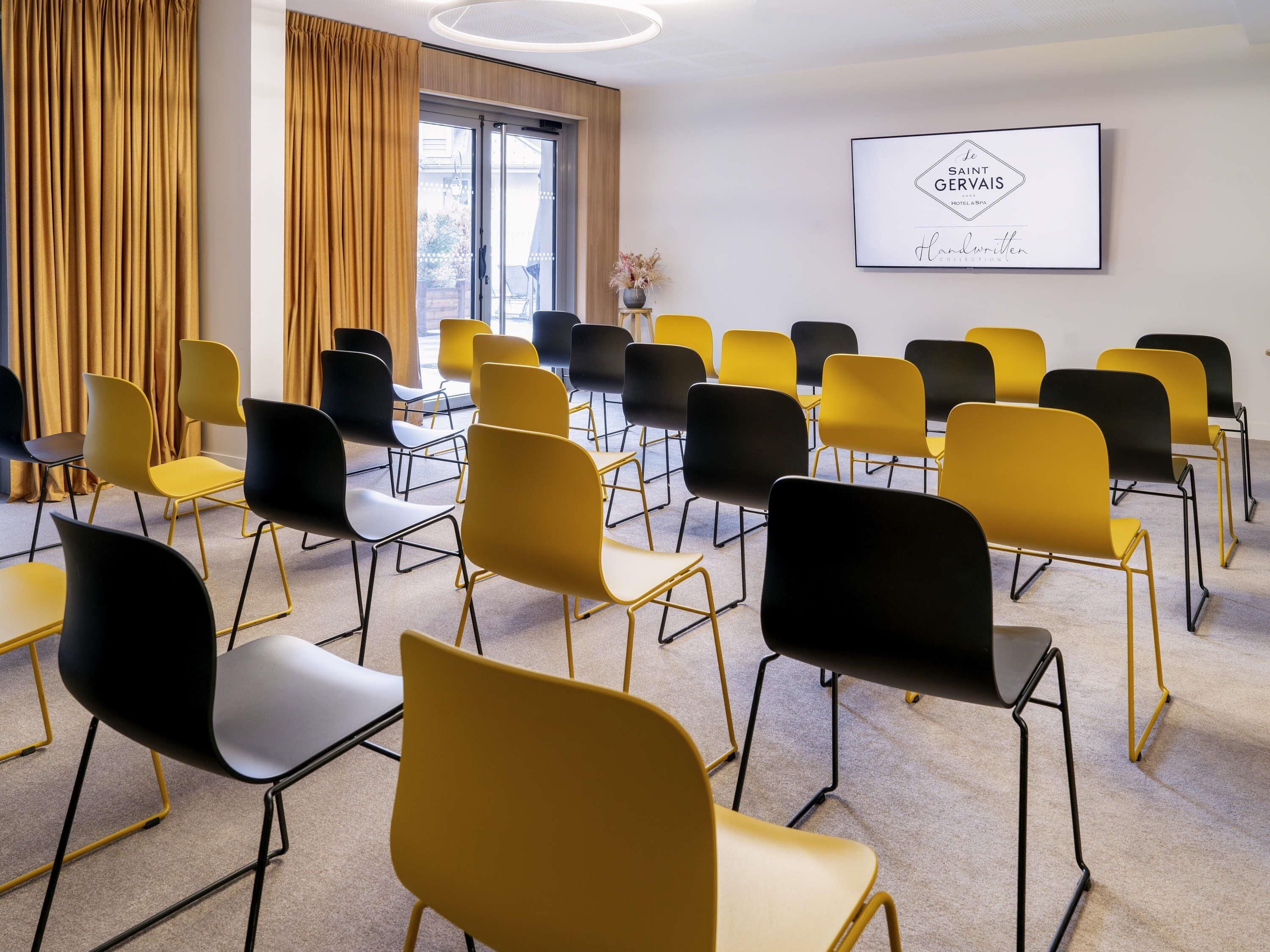 A conference room with rows of chairs, a large window with curtains, and a framed sign on the wall.