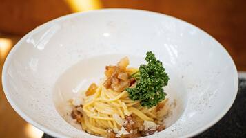Plato blanco con pasta, carne y una guarnición sobre una superficie oscura.