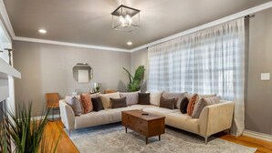 A modern living room with a sectional sofa, a coffee table, and a large window with sheer curtains.