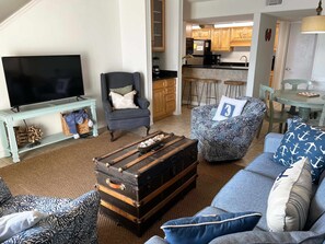 A living room with a television, armchair, patterned sofa, and a vintage suitcase. - Sugar Beach 321 by ALBVR – Beautiful condo & views just steps from the beach! (Orange Beach)