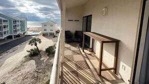 Un balcon avec vue sur la plage, une piscine et un immeuble à la façade blanche.