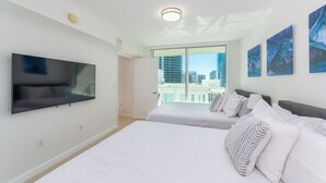 A modern hotel room with a large bed, a flat-screen TV mounted on the wall, and a city view through the window.