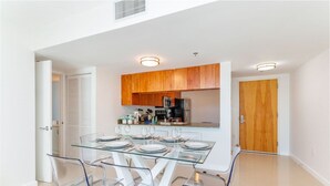 A modern kitchen with wooden cabinets, a glass dining table, and clear chairs.