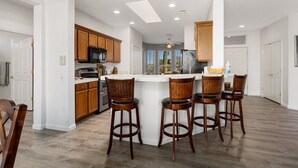 A modern kitchen with wooden cabinets, a central island with bar stools, and a view to the outside. - SUMMER SPECIAL SUN CITY GRAND REMODLED HOME WITH POOL (Surprise)