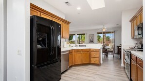 A modern kitchen with wooden cabinets, a black refrigerator, and a large island with a sink. - SUMMER SPECIAL SUN CITY GRAND REMODLED HOME WITH POOL (Surprise)