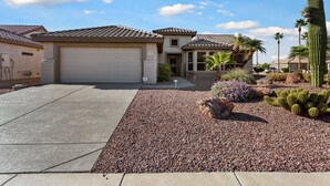 A two-story house with a garage, a gravel driveway, and a desert garden with cacti and a palm tree. - SUMMER SPECIAL SUN CITY GRAND REMODLED HOME WITH POOL (Surprise)