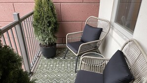 A balcony with two wicker chairs, a potted plant, and a patterned floor. - Modern and Cozy Downtown TC Condo. Walk To Beaches, Bars, Restaurants & More. (Traverse City)