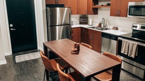 A modern kitchen with wooden cabinets, stainless steel appliances, and a dining area with a table and chairs. - Modern and Cozy Downtown TC Condo. Walk To Beaches, Bars, Restaurants & More. (Traverse City)