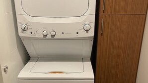A front-loading washing machine with a control panel, a dryer, and a wooden cabinet in a laundry room. - Modern and Cozy Downtown TC Condo. Walk To Beaches, Bars, Restaurants & More. (Traverse City)