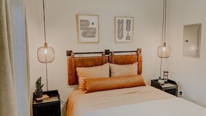 A bedroom with a bed, two bedside tables, a nightstand, a potted plant, and two wall-mounted artworks. - Modern and Cozy Downtown TC Condo. Walk To Beaches, Bars, Restaurants & More. (Traverse City)