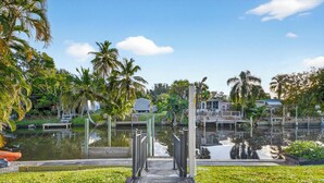 A wooden dock leading to a calm water body, surrounded by lush greenery and palm trees. - SEADREAM WITH LITE BREAKFAST, HOT TUBE, AND CANAL VIEW (Stuart)