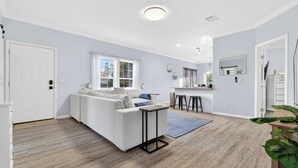 A modern living room with a white sofa, a small table, and a kitchen area in the background. - SEADREAM WITH LITE BREAKFAST, HOT TUBE, AND CANAL VIEW (Stuart)