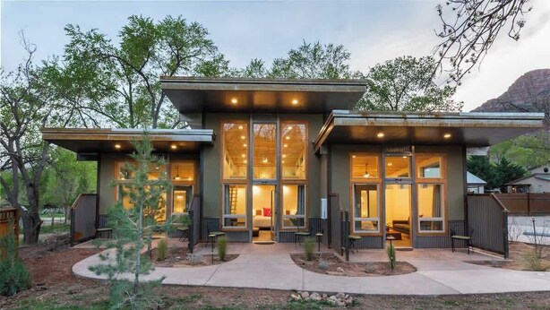 Une maison moderne dotée de grandes fenêtres, d’un patio et offrant une vue sur les montagnes.