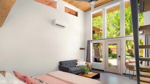 Une chambre moderne comprenant un lit, un canapé, une table basse avec une plante et une grande fenêtre donnant sur un paysage verdoyant.