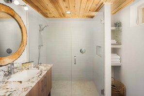 Une salle de bain avec un plafond en bois, une douche en verre, un lavabo avec un plan de toilette en marbre et un miroir avec un cadre en bois.