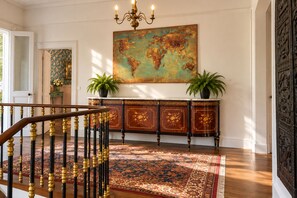 A grand entryway with a wooden staircase, a world map painting, and a decorative cabinet.