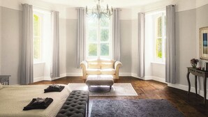 Une chambre spacieuse avec un grand lit, un coin salon avec un fauteuil et un lustre.