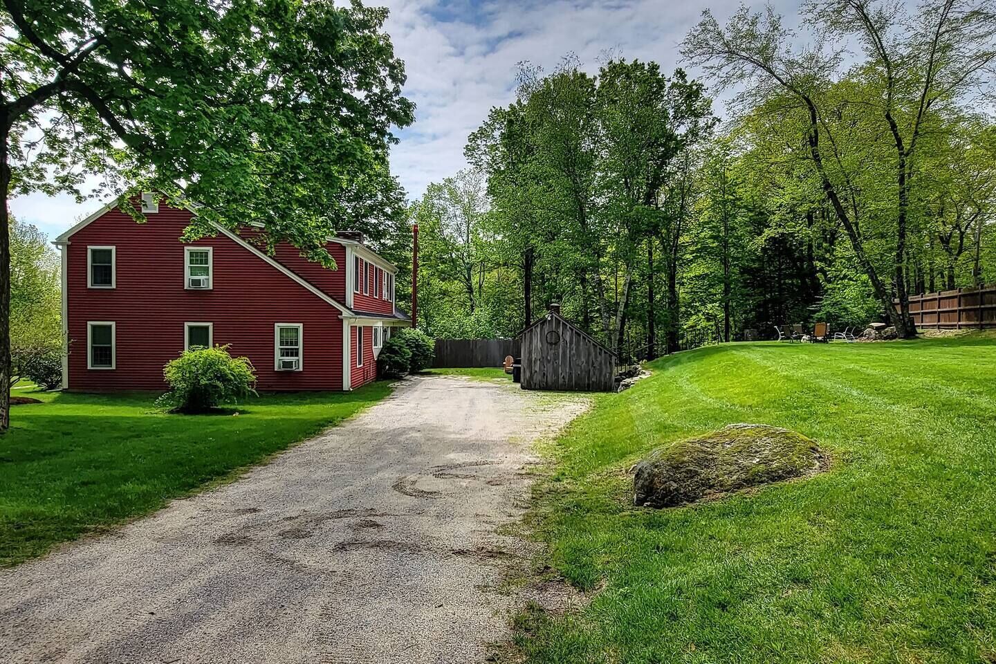 A red two-story house with a gravel driveway leading to a wooden shed.