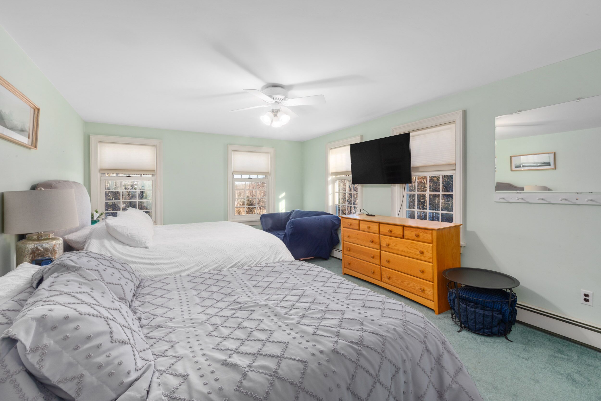 A bedroom with a bed, dresser, TV, and windows.