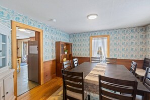 Ein Esszimmer mit Holztisch, Stühlen, einem Schrank und Wandpapier mit Muster.