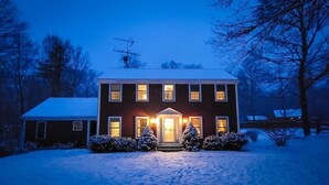 Ein zweistöckiges Haus mit einer schneebedeckten Rasenfläche und einer beleuchteten Eingangstür.