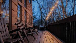A wooden deck with benches, a barbecue grill, and string lights.