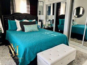 A bedroom with a large bed, a white bench, a mirror, and a wardrobe.