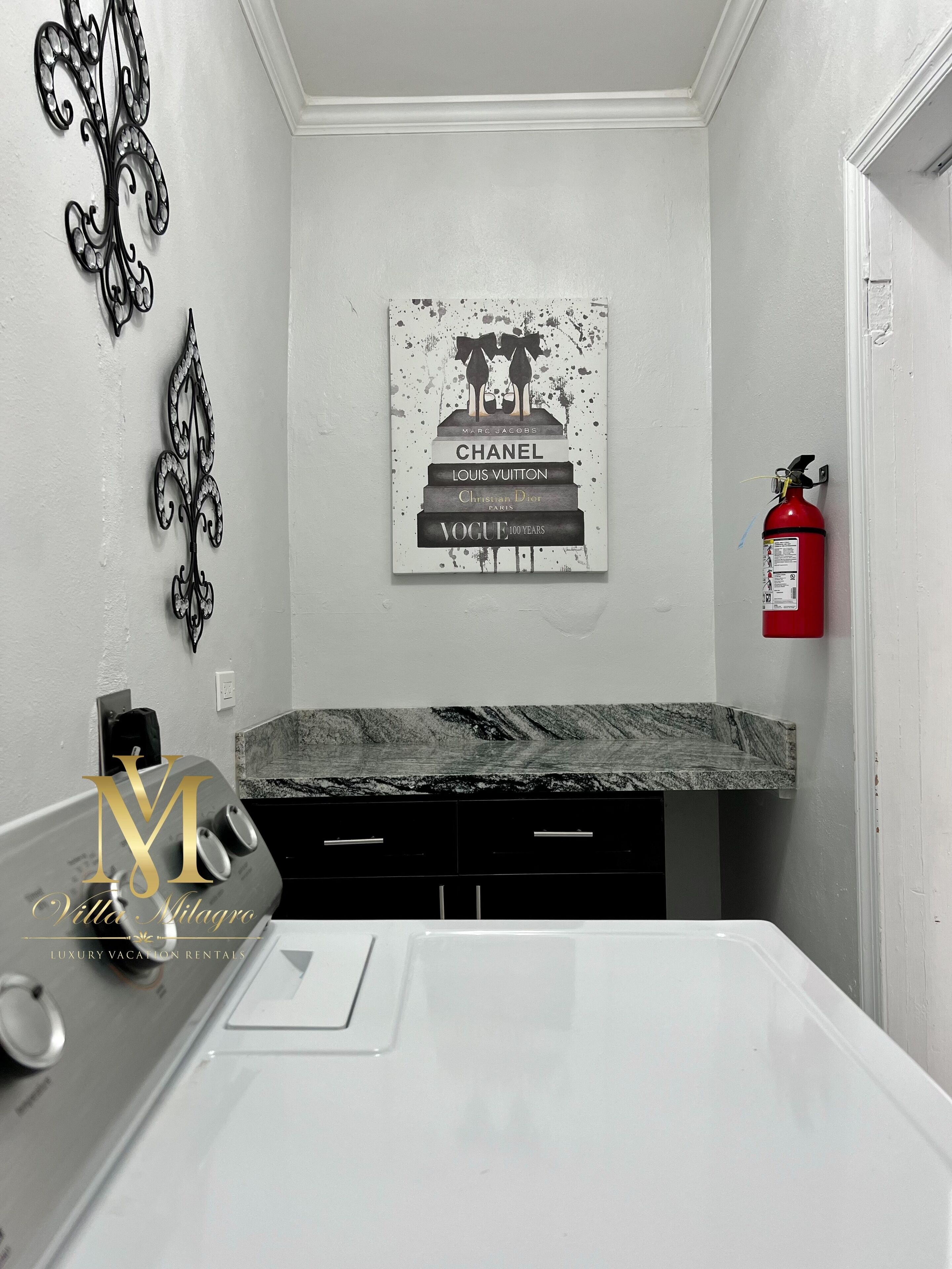 A bathroom with a marble countertop, a framed poster of luxury brands, and a fire extinguisher.