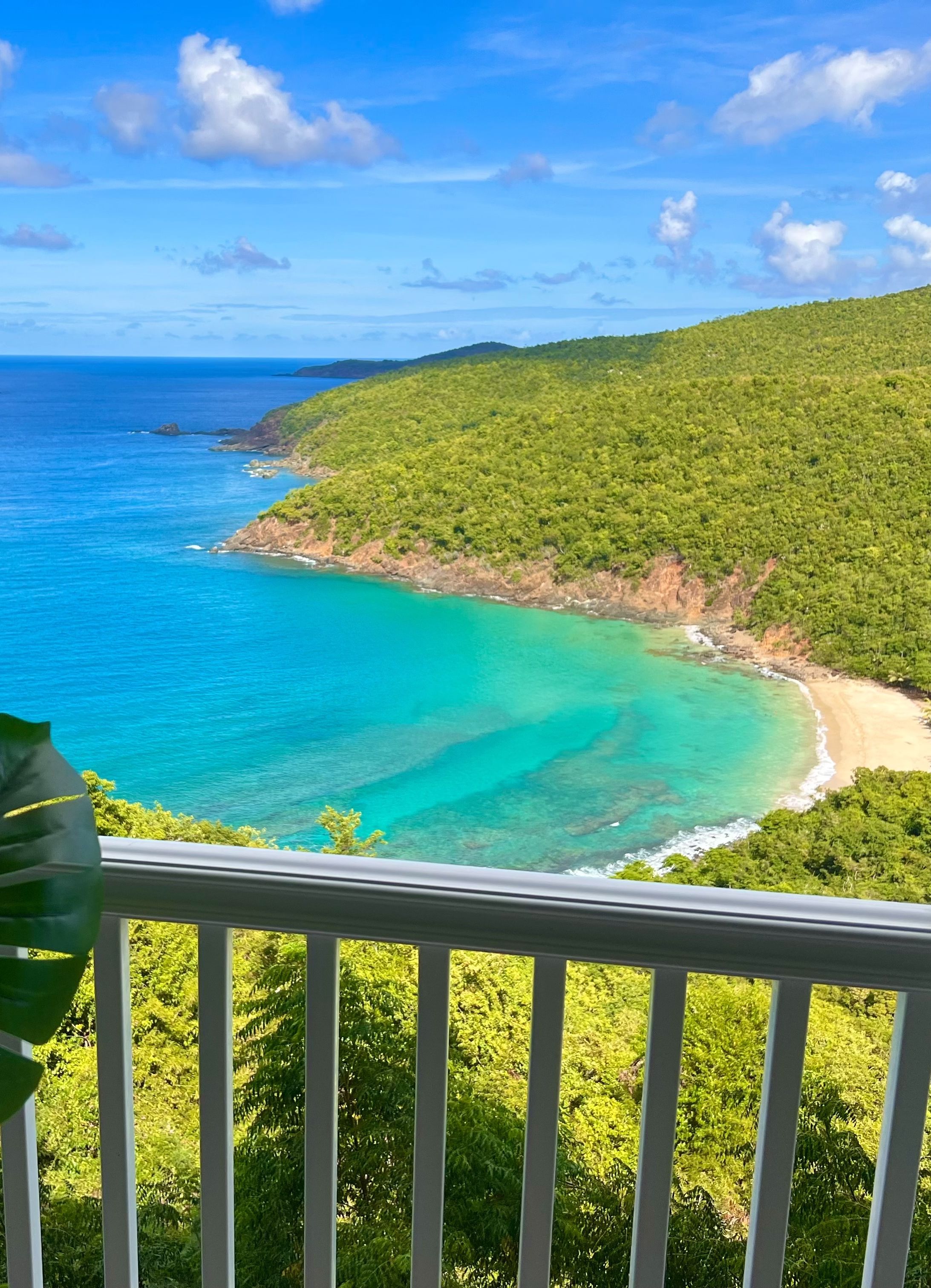 A balcony with a view of a turquoise sea and a green hillside.
