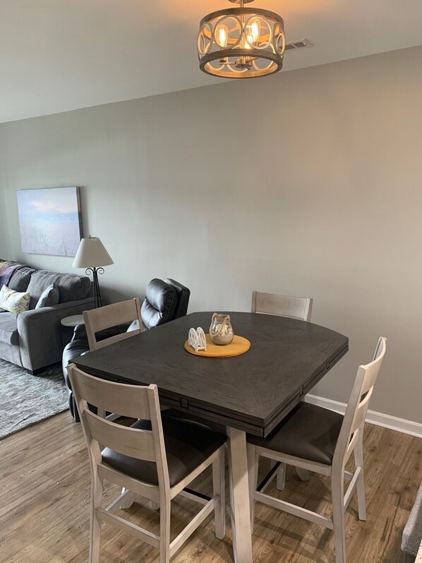 A dining area with a round table, four chairs, a chandelier, and a painting on the wall.