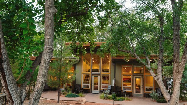 Un bâtiment moderne doté de grandes fenêtres en verre, entouré d’arbres et d’un jardin bien entretenu.