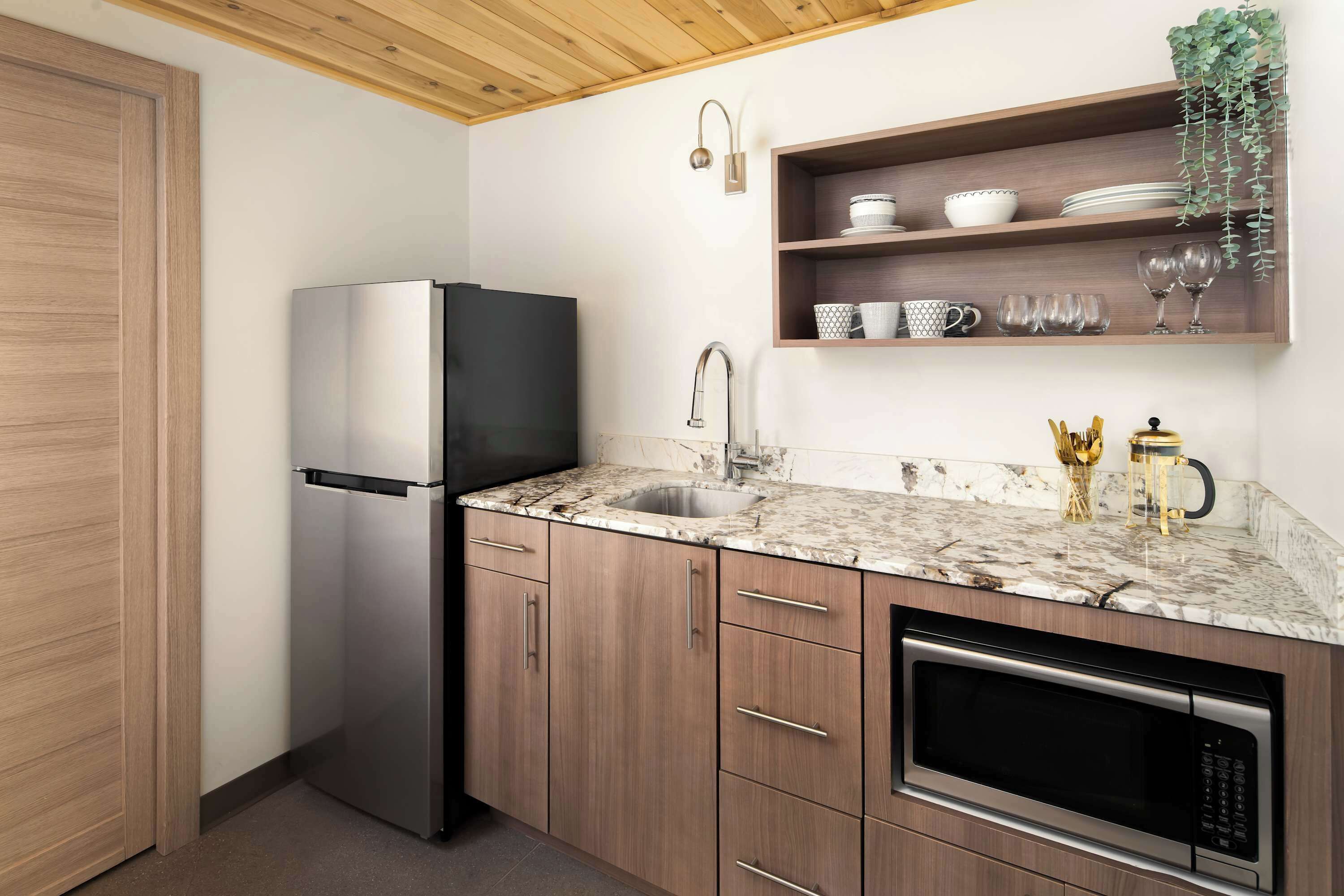A kitchen with a built-in refrigerator, a sink, a microwave, wooden cabinets, and a shelf with kitchenware.