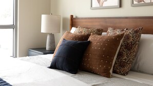 Een net opgemaakt bed met een sprei, kussens en een nachtkastje met een lamp.