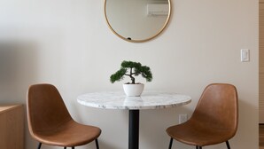 Een ronde tafel met een bonsai in pot, twee bruine stoelen, een ronde spiegel en een zwarte voet.
