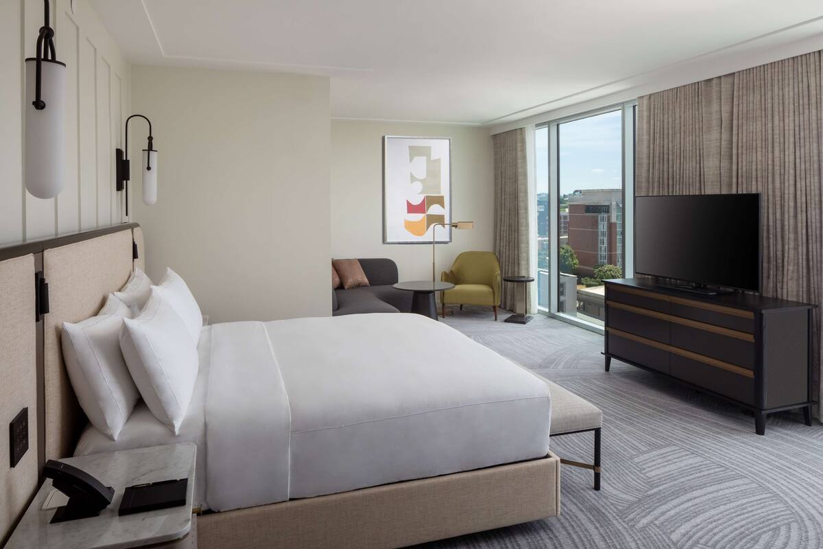 A modern hotel room with a large bed, a TV, a small table, and a chair.